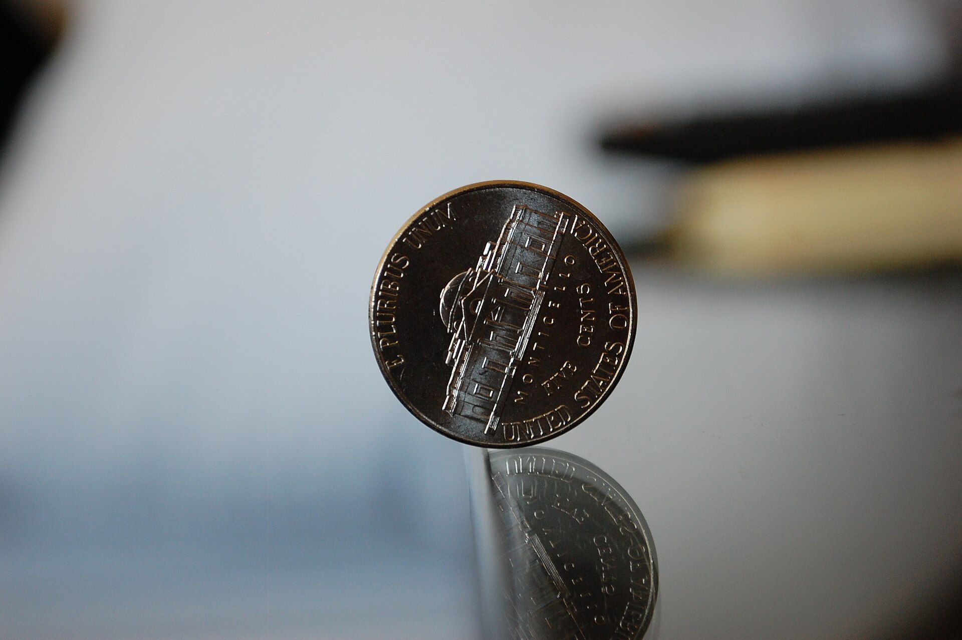A real Jefferson nickel balanced upright on the edge of a glass table